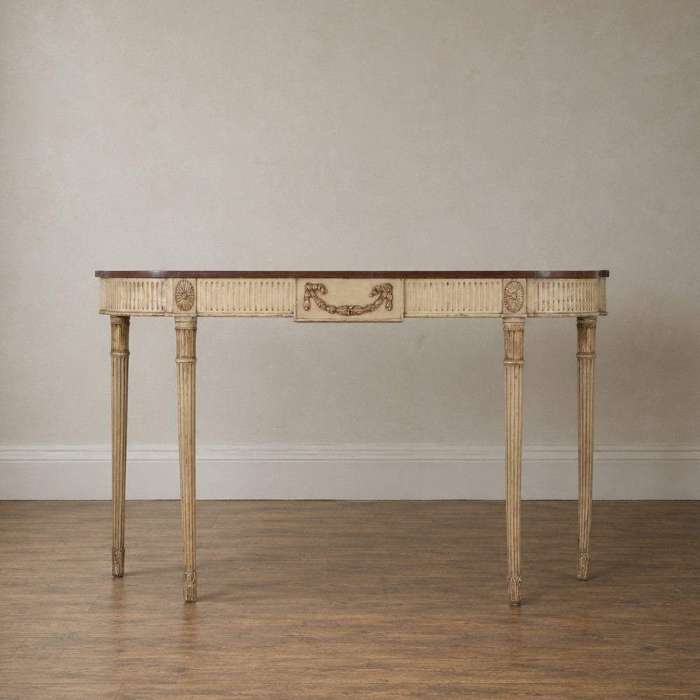 A Georgian style painted cream and gilt console table featuring a dark wood top, fluted legs, and carved swag detailing.