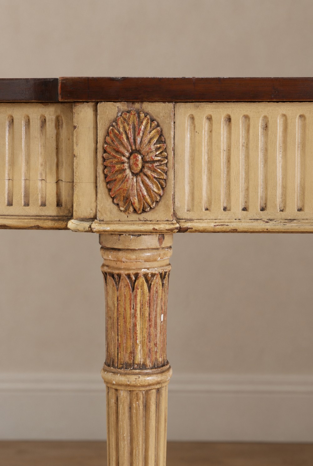 A Georgian style painted cream and gilt console table featuring a dark wood top, fluted legs, and carved swag detailing. View V