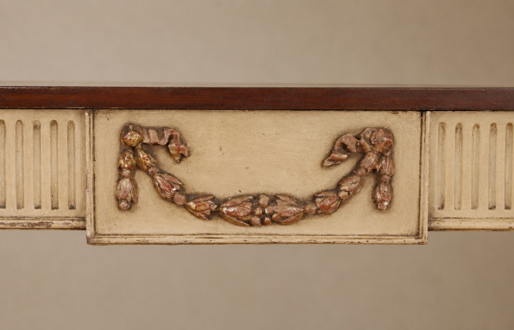 A Georgian style painted cream and gilt console table featuring a dark wood top, fluted legs, and carved swag detailing. View VI