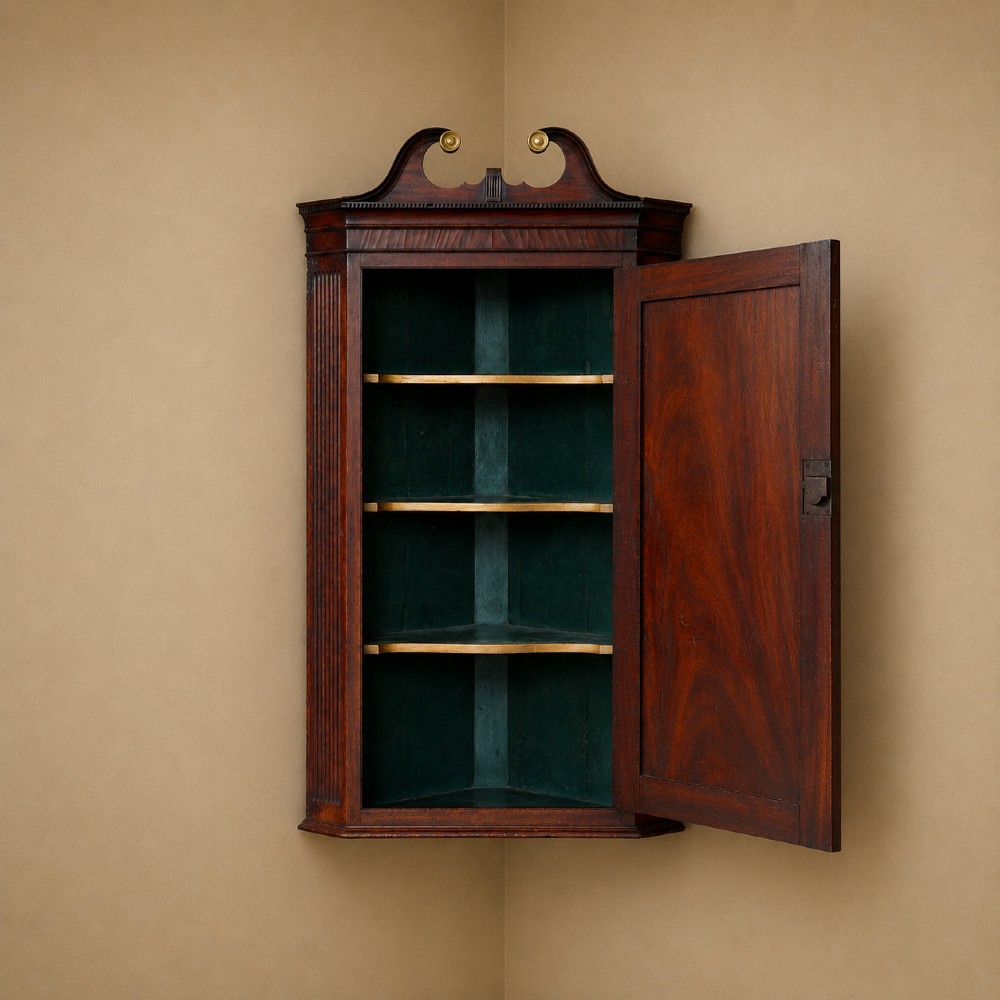 A Georgian dark mahogany hanging corner cupboard featuring a swan-neck pediment with brass paterae and a single panelled door with a brass escutcheon. View II
