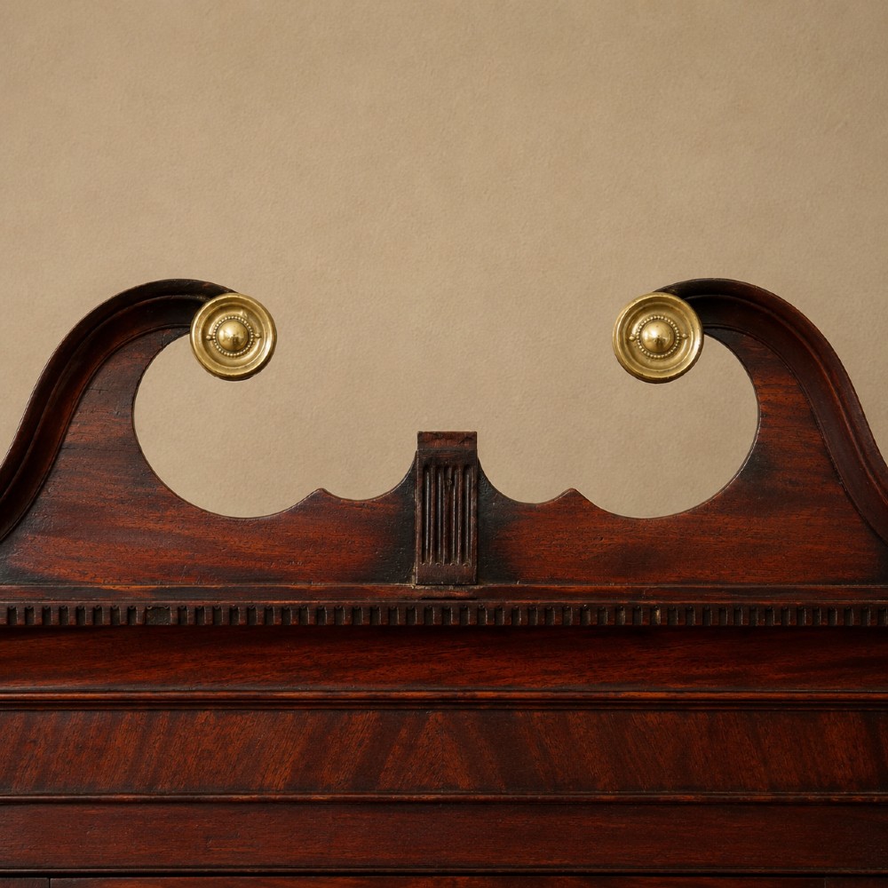 A Georgian dark mahogany hanging corner cupboard featuring a swan-neck pediment with brass paterae and a single panelled door with a brass escutcheon. View V
