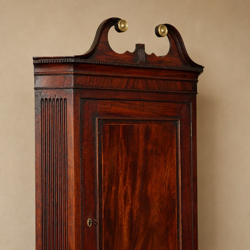 A Georgian dark mahogany hanging corner cupboard featuring a swan-neck pediment with brass paterae and a single panelled door with a brass escutcheon. View VI