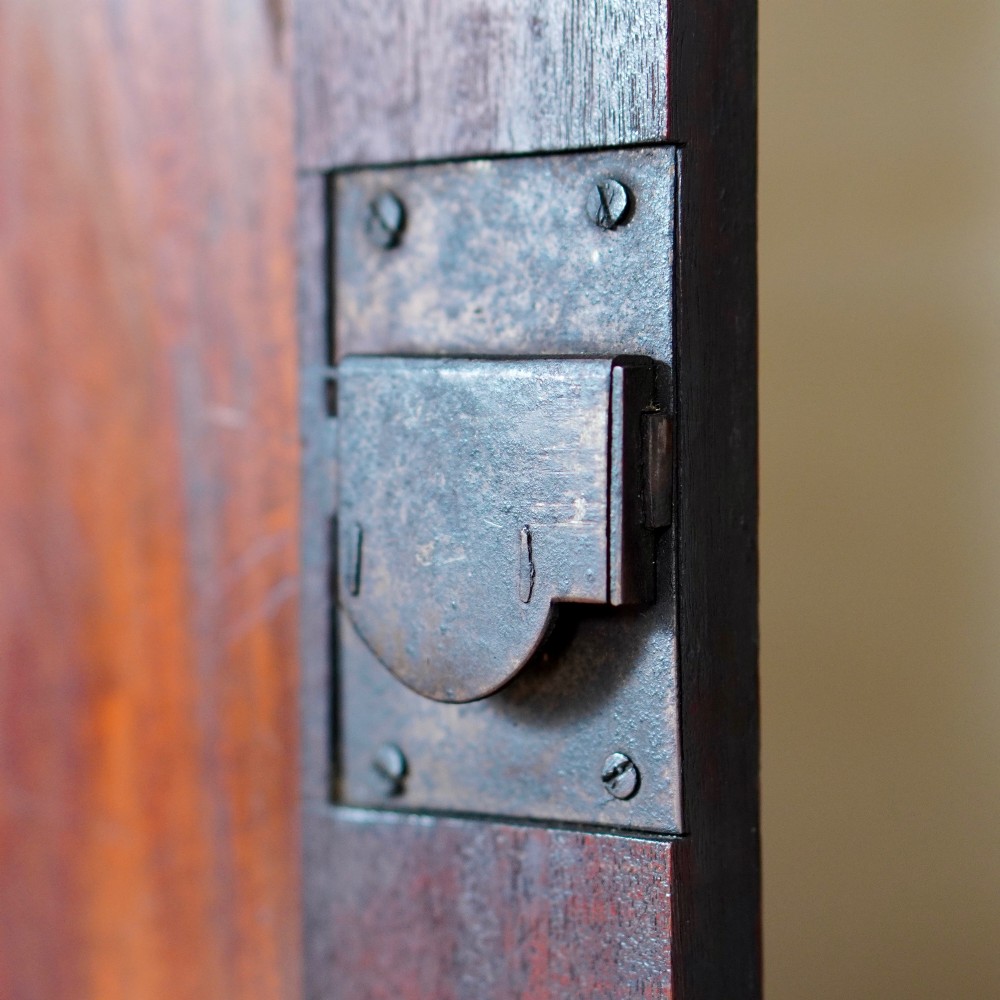 A Georgian dark mahogany hanging corner cupboard featuring a swan-neck pediment with brass paterae and a single panelled door with a brass escutcheon. View VII