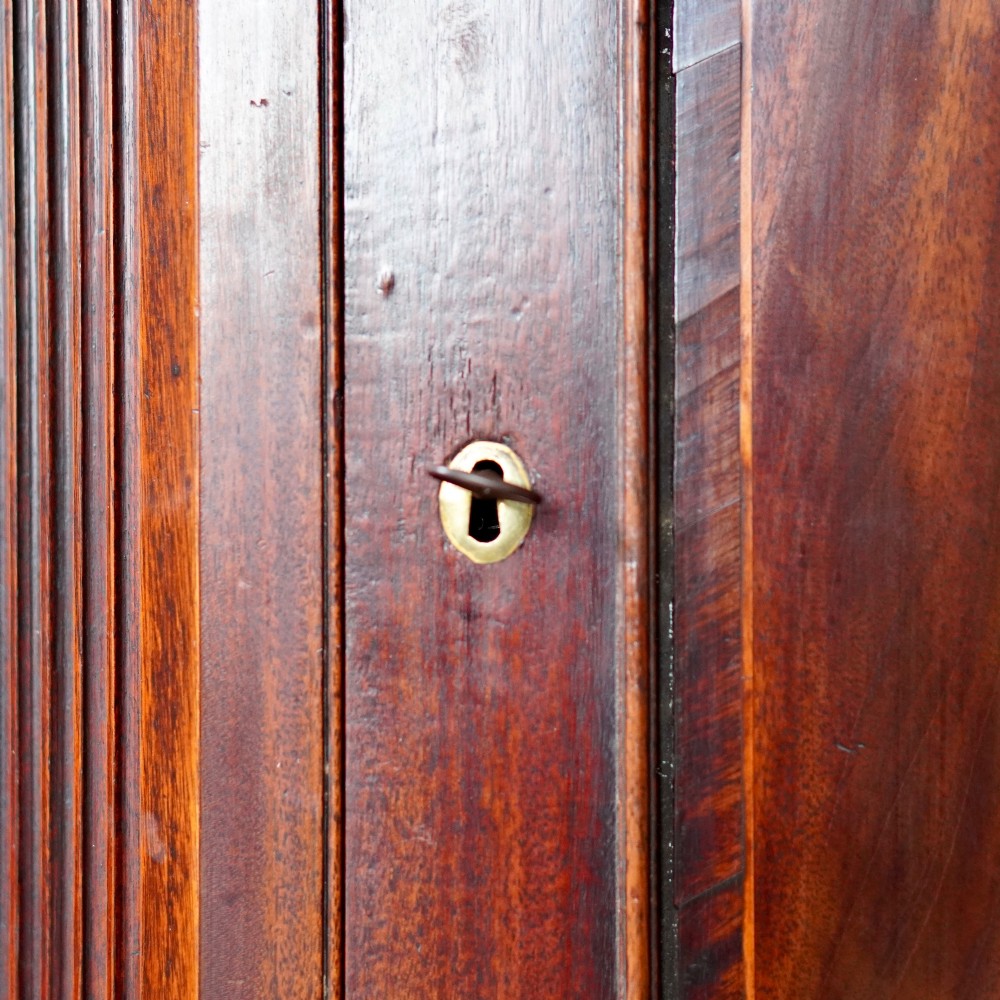 A Georgian dark mahogany hanging corner cupboard featuring a swan-neck pediment with brass paterae and a single panelled door with a brass escutcheon. View IX