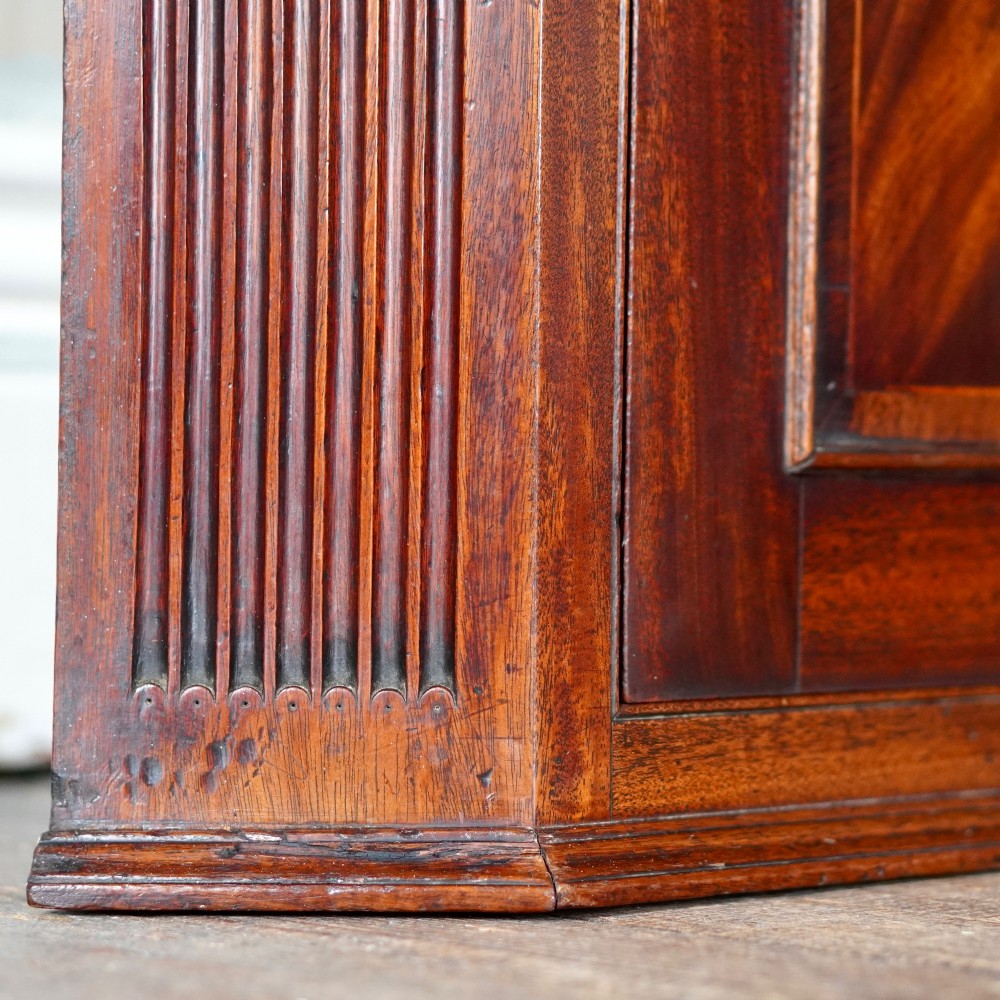 A Georgian dark mahogany hanging corner cupboard featuring a swan-neck pediment with brass paterae and a single panelled door with a brass escutcheon. View X