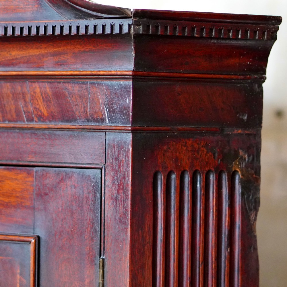 A Georgian dark mahogany hanging corner cupboard featuring a swan-neck pediment with brass paterae and a single panelled door with a brass escutcheon. View XI