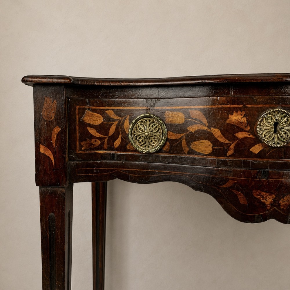 An 18th-century Dutch walnut side table featuring a serpentine front, floral marquetry inlay, a single drawer, and four square tapered legs. View VI