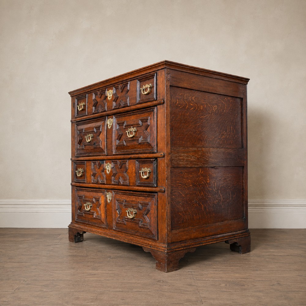 An early eighteenth-century oak chest of drawers featuring four drawers decorated with geometric applied mouldings and brass drop handles. View II