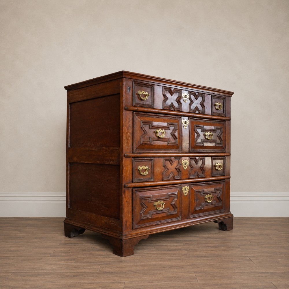 An early eighteenth-century oak chest of drawers featuring four drawers decorated with geometric applied mouldings and brass drop handles. View VI