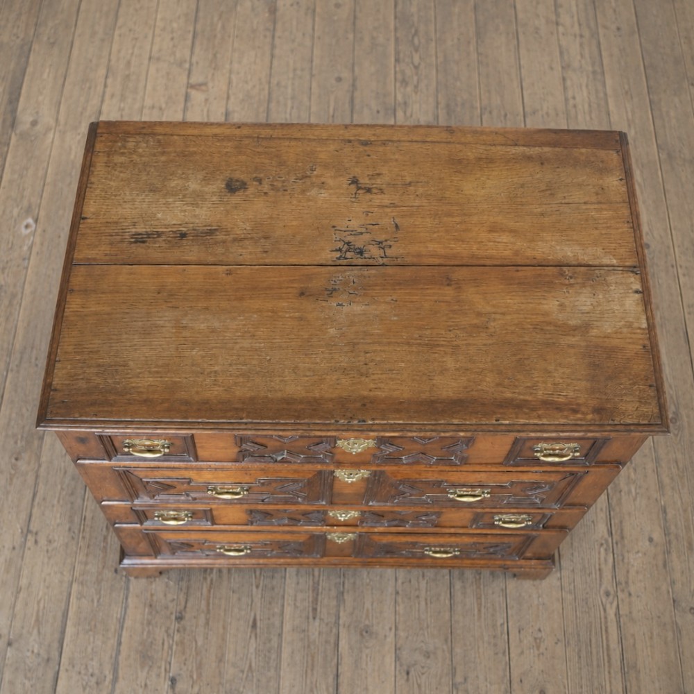 An early eighteenth-century oak chest of drawers featuring four drawers decorated with geometric applied mouldings and brass drop handles. View VII