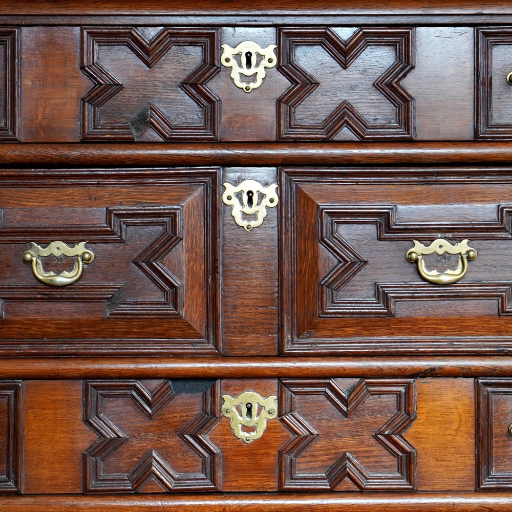 An early eighteenth-century oak chest of drawers featuring four drawers decorated with geometric applied mouldings and brass drop handles. View IX