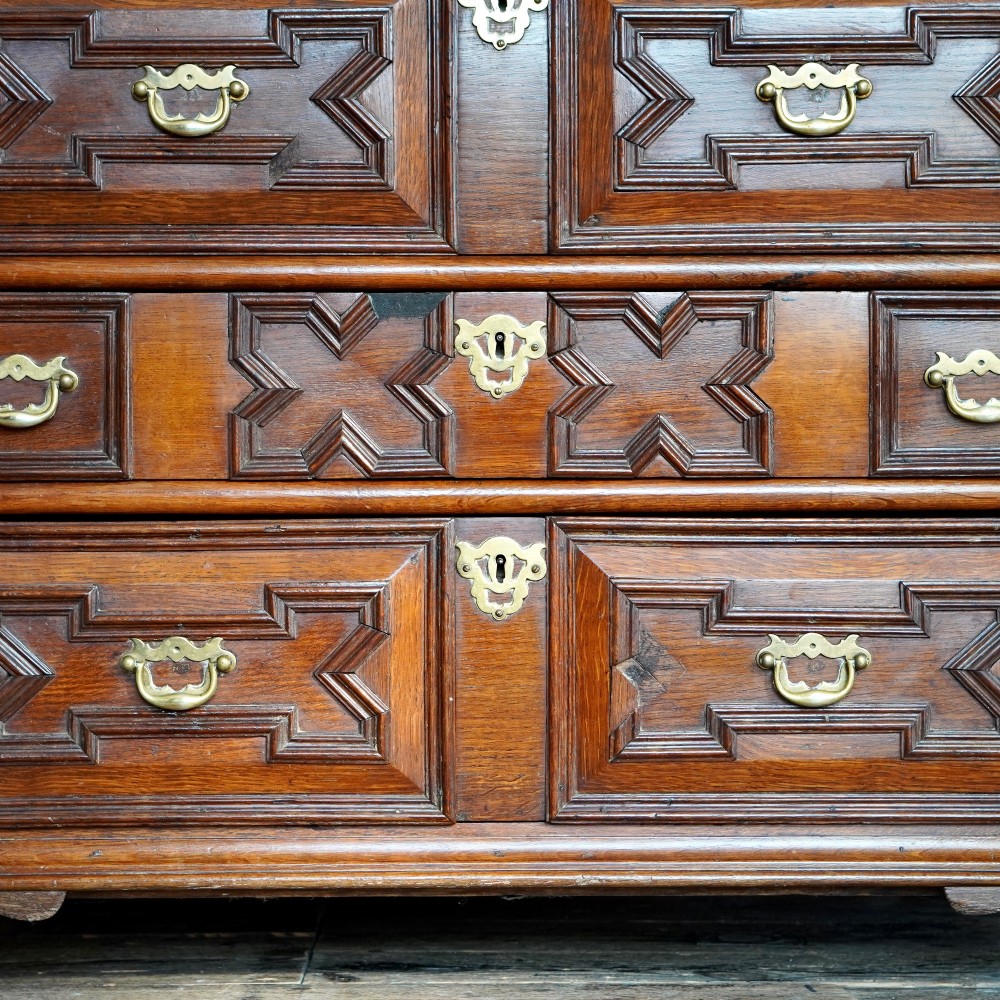An early eighteenth-century oak chest of drawers featuring four drawers decorated with geometric applied mouldings and brass drop handles. View X