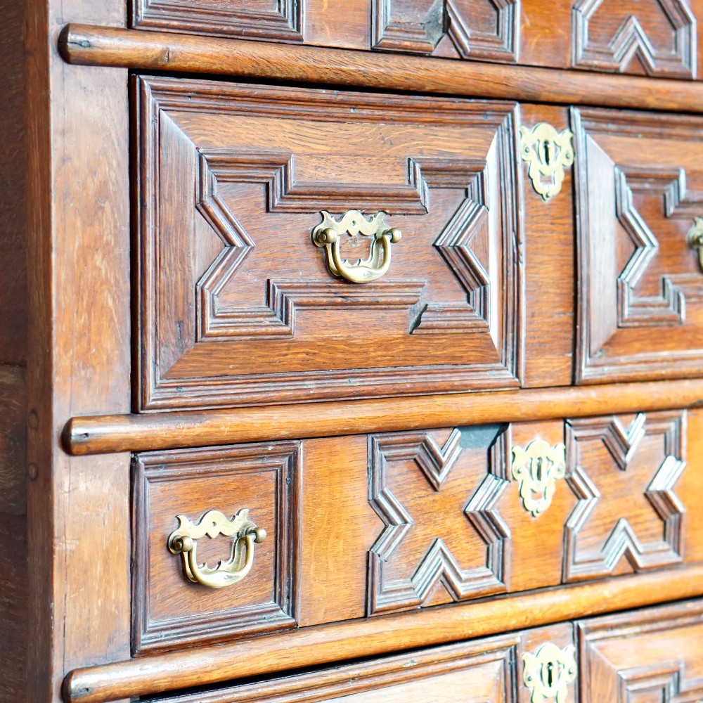 An early eighteenth-century oak chest of drawers featuring four drawers decorated with geometric applied mouldings and brass drop handles. View XI