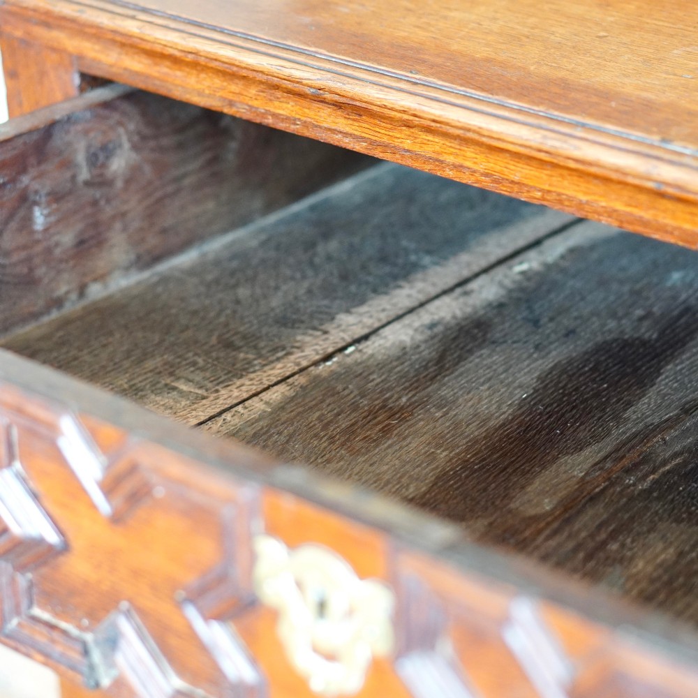 An early eighteenth-century oak chest of drawers featuring four drawers decorated with geometric applied mouldings and brass drop handles. View XV