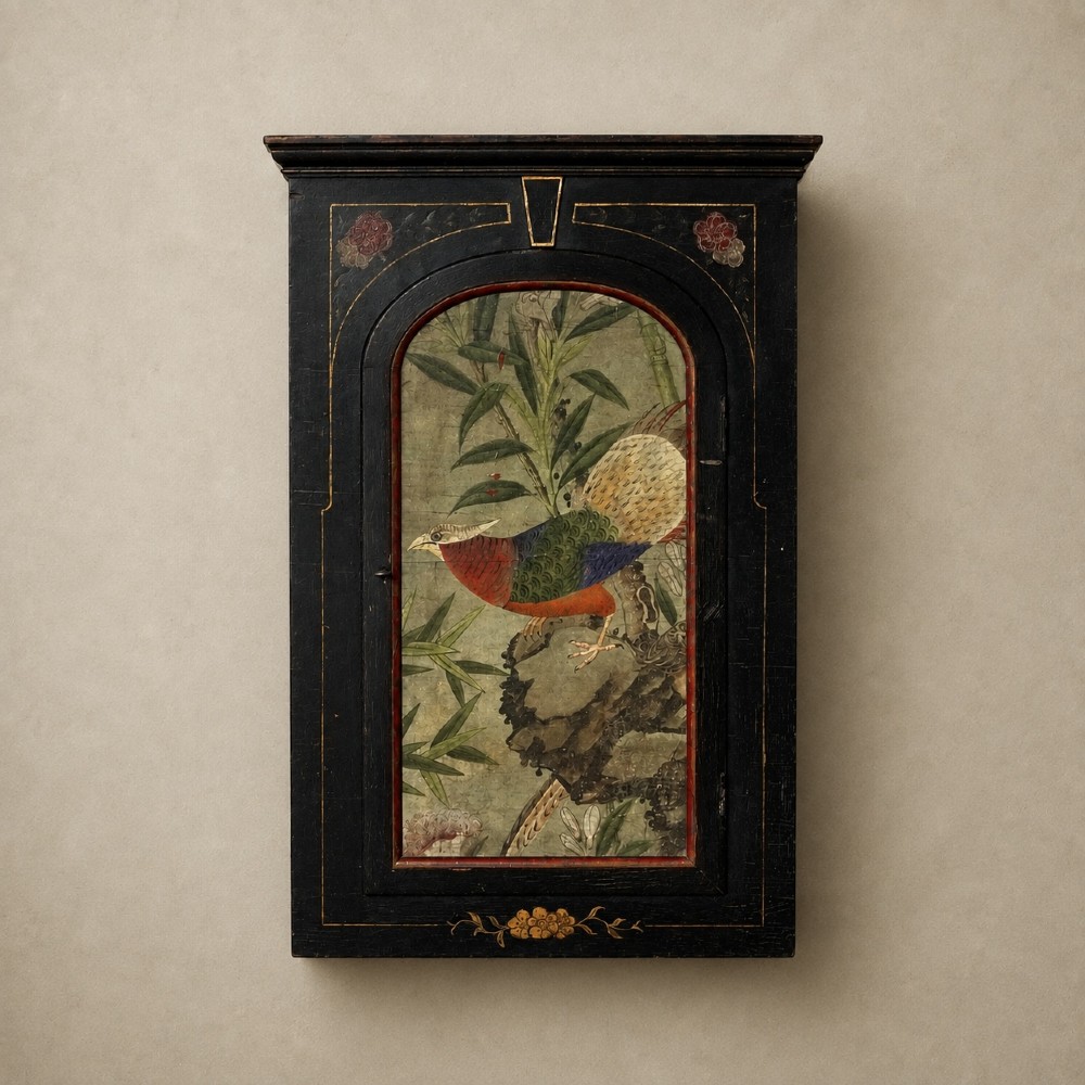 An ebonised black wooden wall cabinet featuring an arched door panel decorated with a hand-painted exotic bird amongst green foliage.