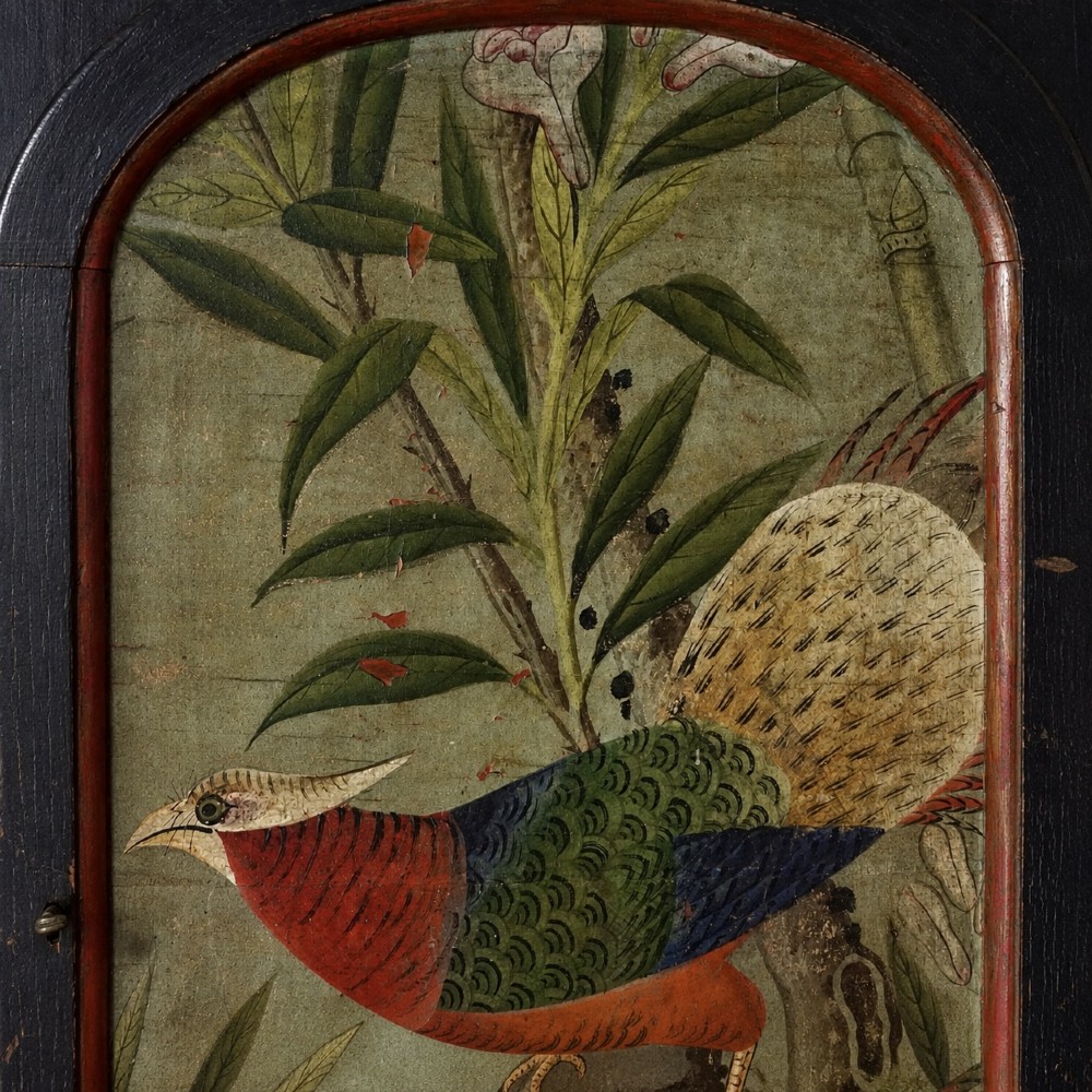 An ebonised black wooden wall cabinet featuring an arched door panel decorated with a hand-painted exotic bird amongst green foliage. View X