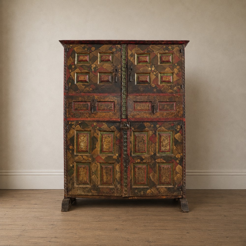 A tall seventeenth-century Spanish oak press cupboard featuring double upper and lower doors decorated with geometric raised panels and painted polychrome geometric patterns.