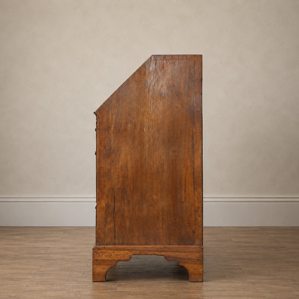 An Early Georgian walnut bureau featuring a sloping drop-front writing lid, four graduated drawers with brass drop handles, and bracket feet. View VI