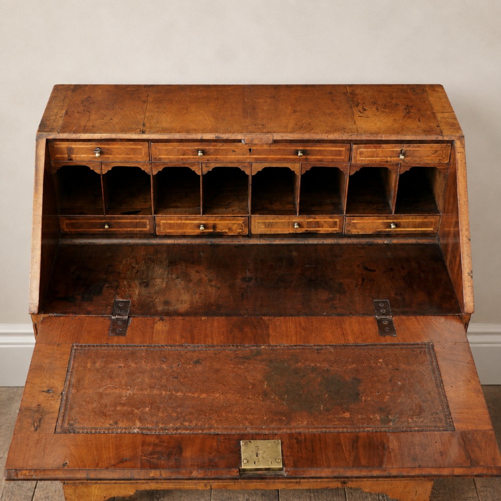 An Early Georgian walnut bureau featuring a sloping drop-front writing lid, four graduated drawers with brass drop handles, and bracket feet. View IX