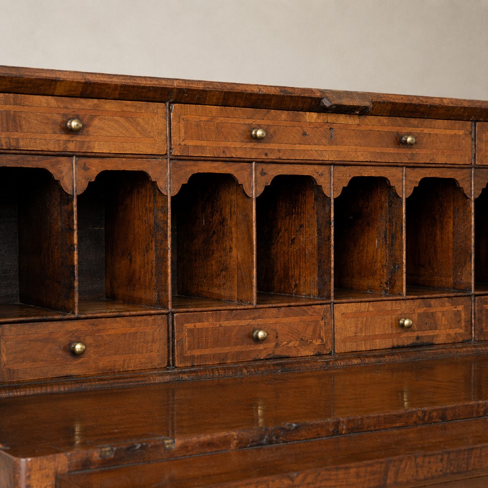 An Early Georgian walnut bureau featuring a sloping drop-front writing lid, four graduated drawers with brass drop handles, and bracket feet. View X