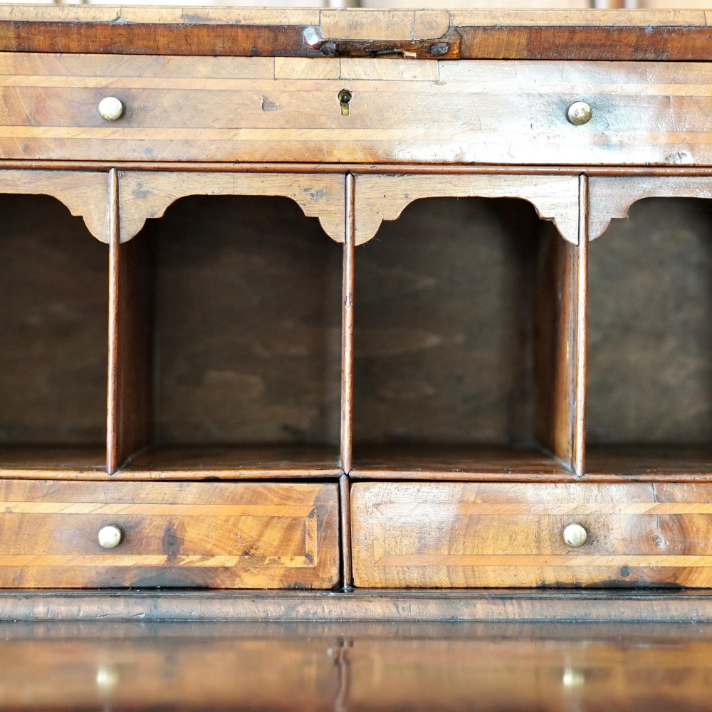 An Early Georgian walnut bureau featuring a sloping drop-front writing lid, four graduated drawers with brass drop handles, and bracket feet. View XI