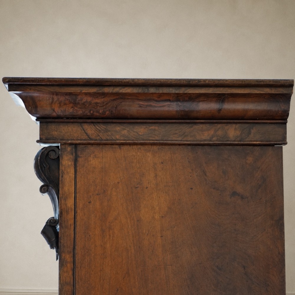 A Victorian single-door wardrobe crafted from figured walnut wood, featuring a central arch-topped mirror panel, carved corbels, and a heavy moulded cornice. View VII