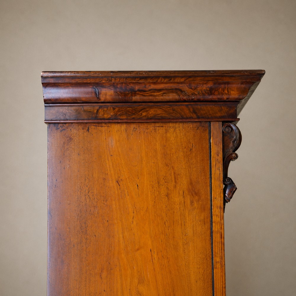 A Victorian single-door wardrobe crafted from figured walnut wood, featuring a central arch-topped mirror panel, carved corbels, and a heavy moulded cornice. View X