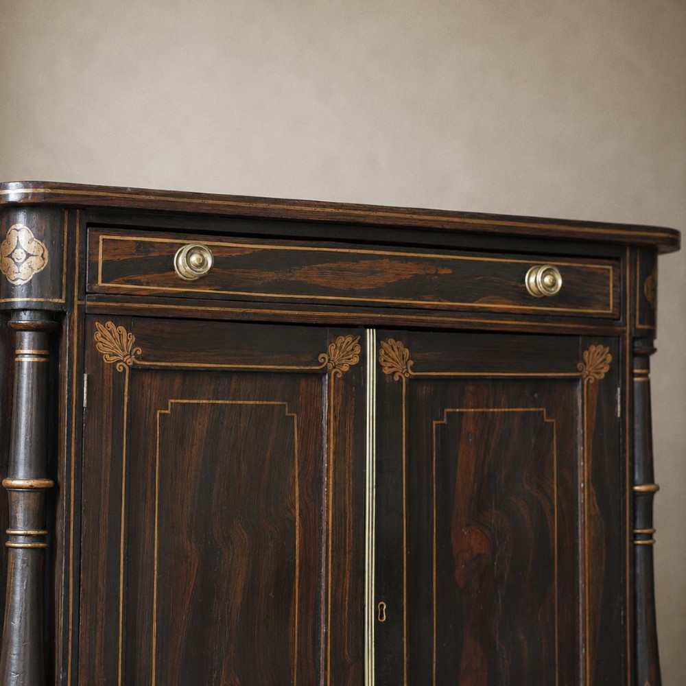A Regency period side cabinet featuring simulated rosewood graining, gilt corner decorations, turned flanking columns, a top drawer, and two cupboard doors. View IX