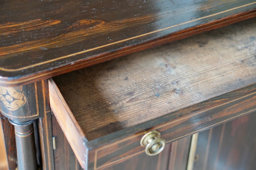A Regency period side cabinet featuring simulated rosewood graining, gilt corner decorations, turned flanking columns, a top drawer, and two cupboard doors. View XIII