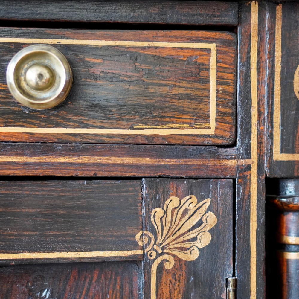 A Regency period side cabinet featuring simulated rosewood graining, gilt corner decorations, turned flanking columns, a top drawer, and two cupboard doors. View XV