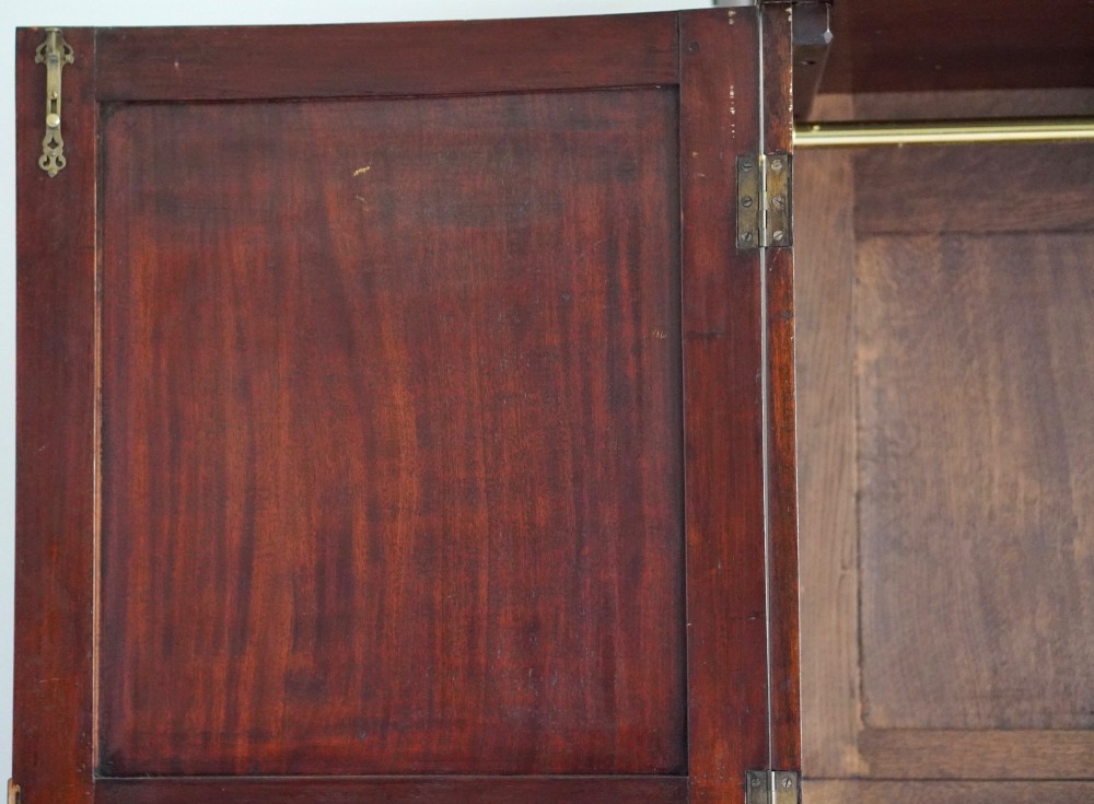 A George III bowfront mahogany wardrobe featuring twin panelled doors with oval flame mahogany veneers above two drawers and flared bracket feet. View VI