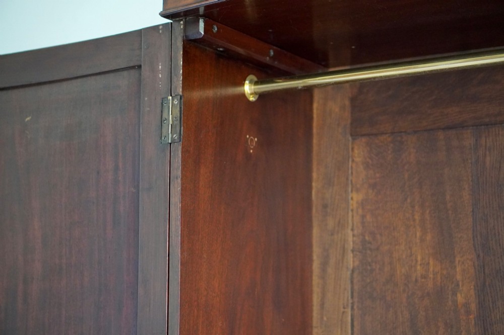 A George III bowfront mahogany wardrobe featuring twin panelled doors with oval flame mahogany veneers above two drawers and flared bracket feet. View VII