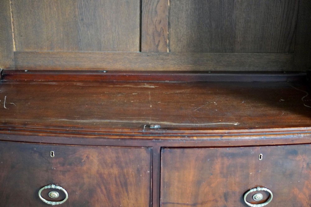 A George III bowfront mahogany wardrobe featuring twin panelled doors with oval flame mahogany veneers above two drawers and flared bracket feet. View VIII