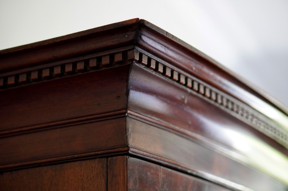 A George III bowfront mahogany wardrobe featuring twin panelled doors with oval flame mahogany veneers above two drawers and flared bracket feet. View XI