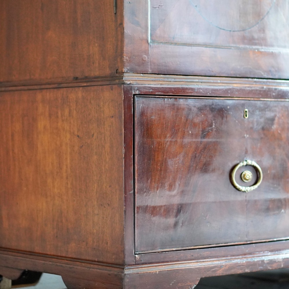 A George III bowfront mahogany wardrobe featuring twin panelled doors with oval flame mahogany veneers above two drawers and flared bracket feet. View XV
