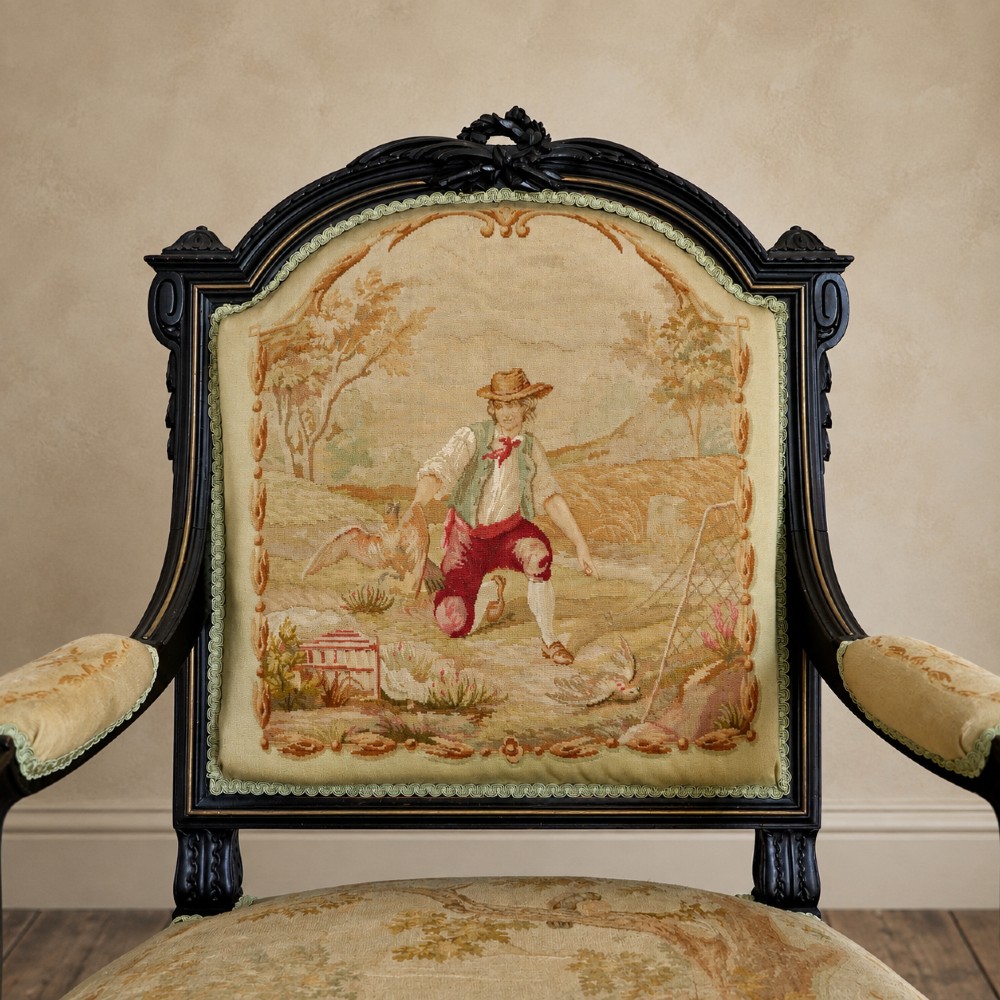 A pair of ebonised beech Louis XVI Revival salon armchairs featuring carved frames, fluted legs, padded armrests, and tapestry upholstery, accompanied by matching footstools. View VI