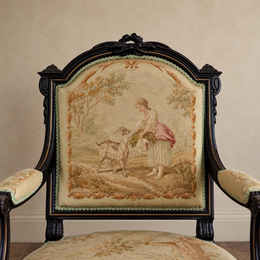 A pair of ebonised beech Louis XVI Revival salon armchairs featuring carved frames, fluted legs, padded armrests, and tapestry upholstery, accompanied by matching footstools. View VII