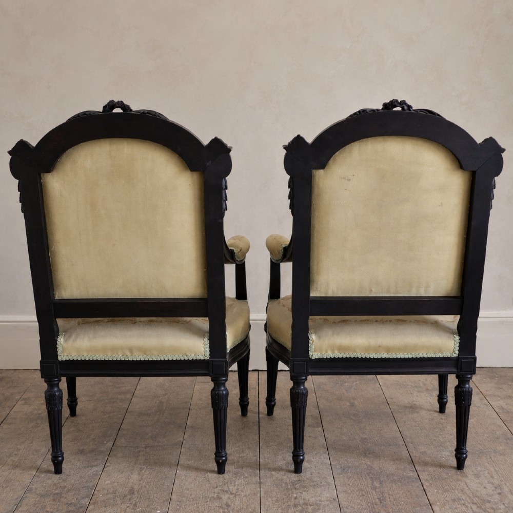A pair of ebonised beech Louis XVI Revival salon armchairs featuring carved frames, fluted legs, padded armrests, and tapestry upholstery, accompanied by matching footstools. View XIV