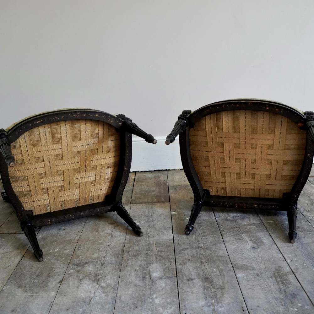 A pair of ebonised beech Louis XVI Revival salon armchairs featuring carved frames, fluted legs, padded armrests, and tapestry upholstery, accompanied by matching footstools. View XV