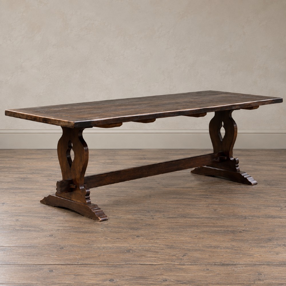 An early twentieth-century dark oak refectory dining table featuring a plank top, pierced trestle end supports, and a central connecting stretcher.