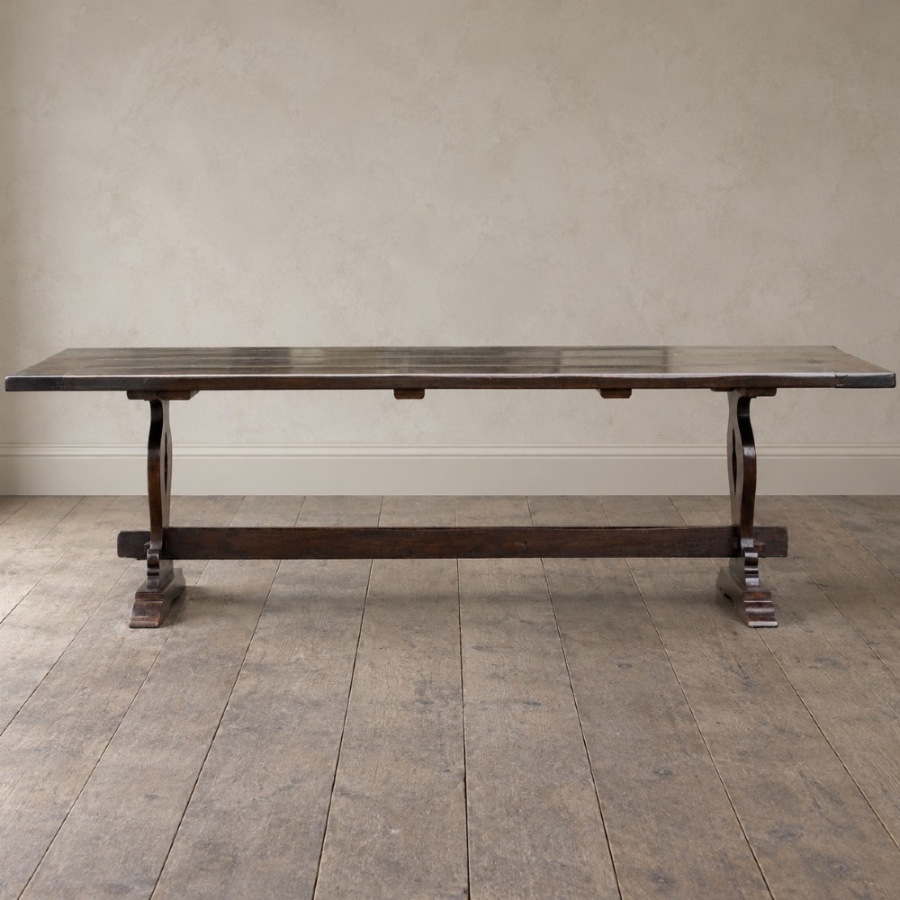 An early twentieth-century dark oak refectory dining table featuring a plank top, pierced trestle end supports, and a central connecting stretcher. View II