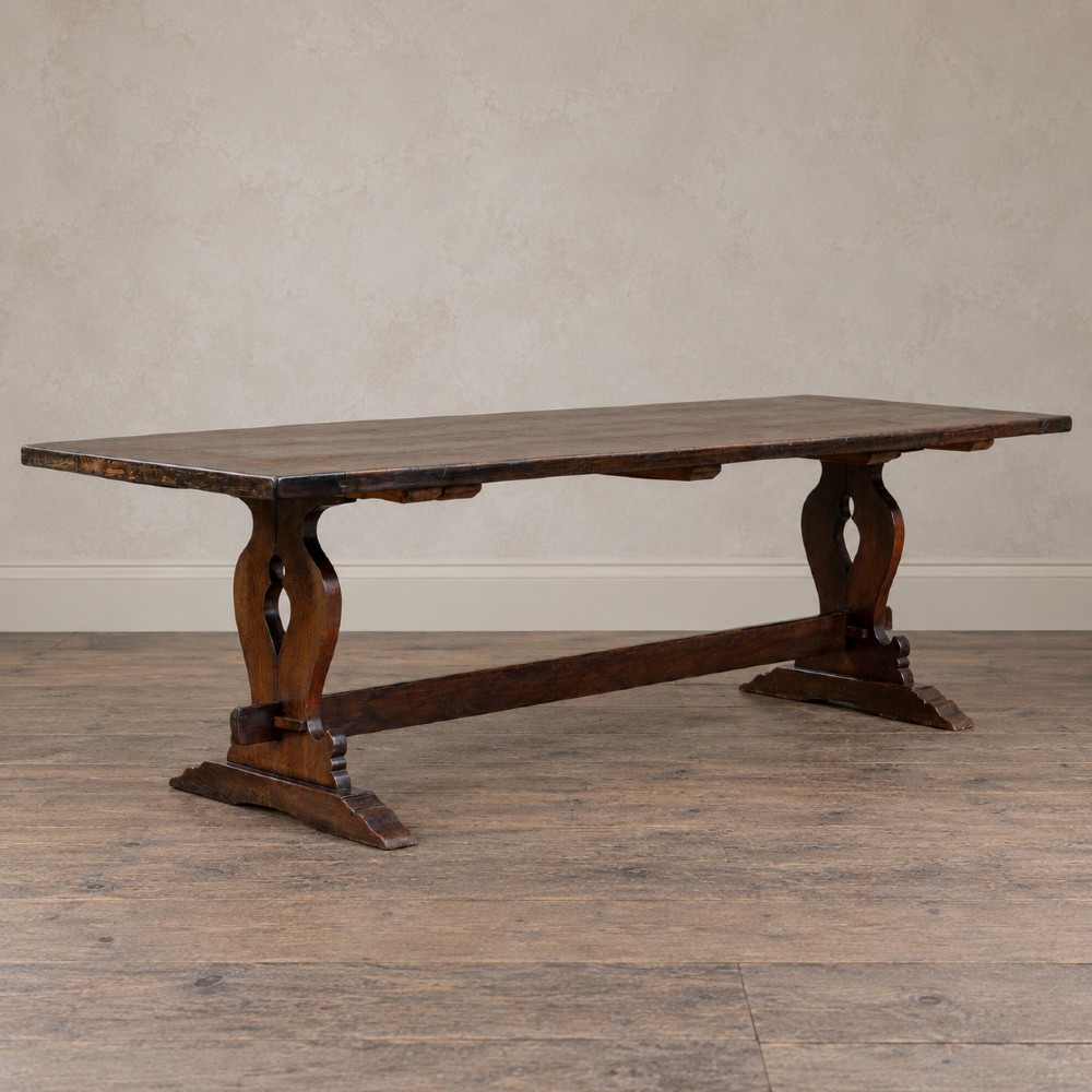 An early twentieth-century dark oak refectory dining table featuring a plank top, pierced trestle end supports, and a central connecting stretcher. View III