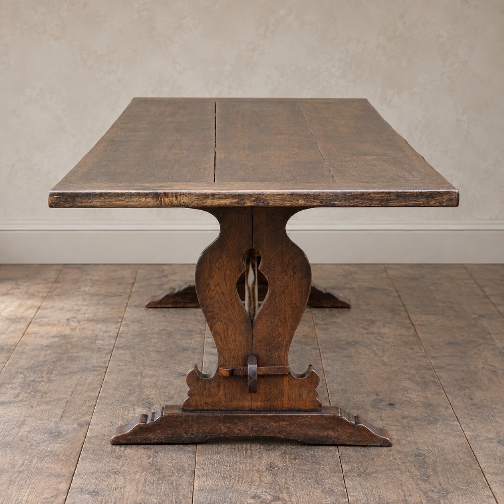 An early twentieth-century dark oak refectory dining table featuring a plank top, pierced trestle end supports, and a central connecting stretcher. View IV