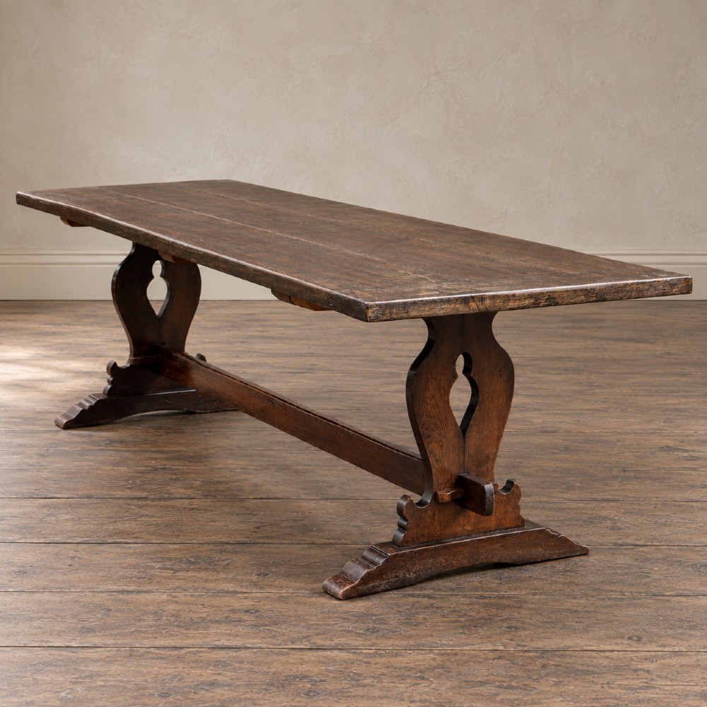 An early twentieth-century dark oak refectory dining table featuring a plank top, pierced trestle end supports, and a central connecting stretcher. View V