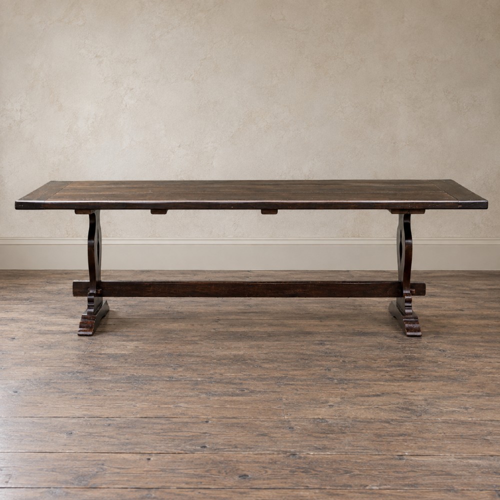 An early twentieth-century dark oak refectory dining table featuring a plank top, pierced trestle end supports, and a central connecting stretcher. View VI