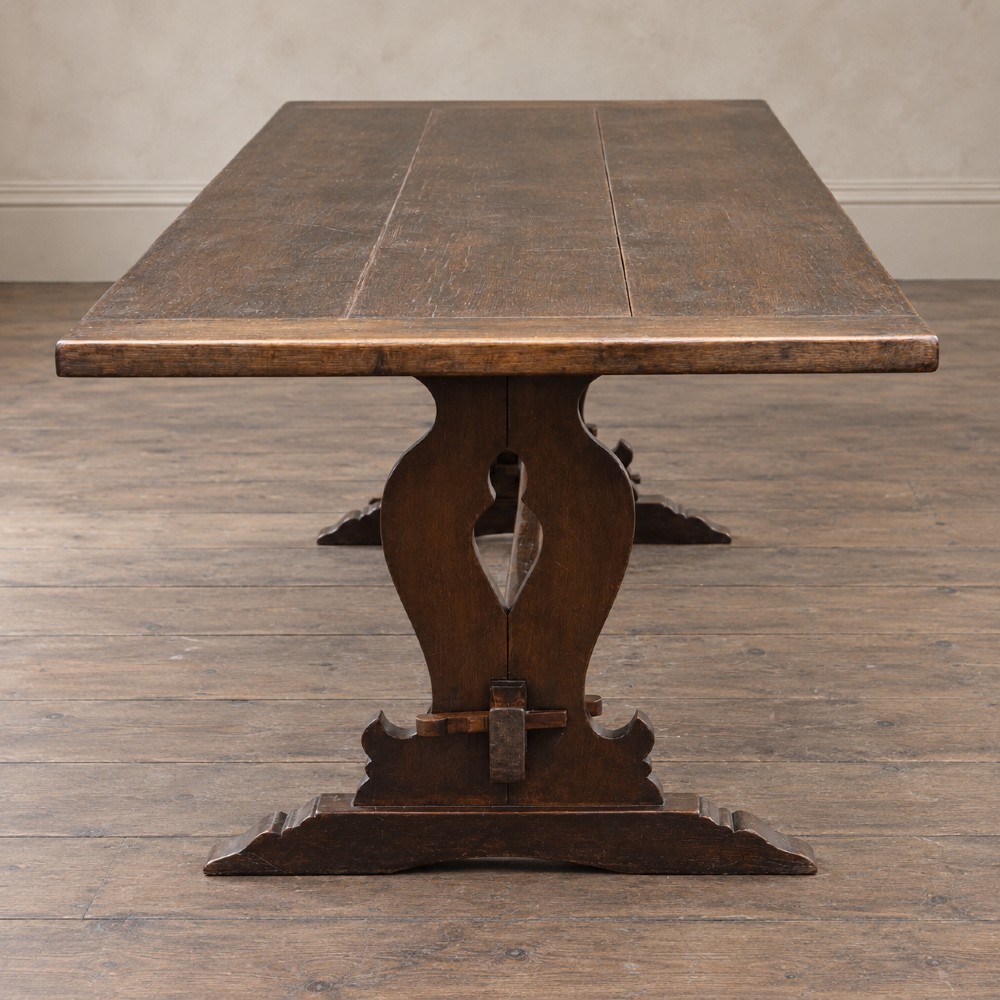 An early twentieth-century dark oak refectory dining table featuring a plank top, pierced trestle end supports, and a central connecting stretcher. View VII