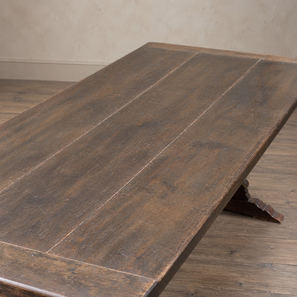 An early twentieth-century dark oak refectory dining table featuring a plank top, pierced trestle end supports, and a central connecting stretcher. View IX