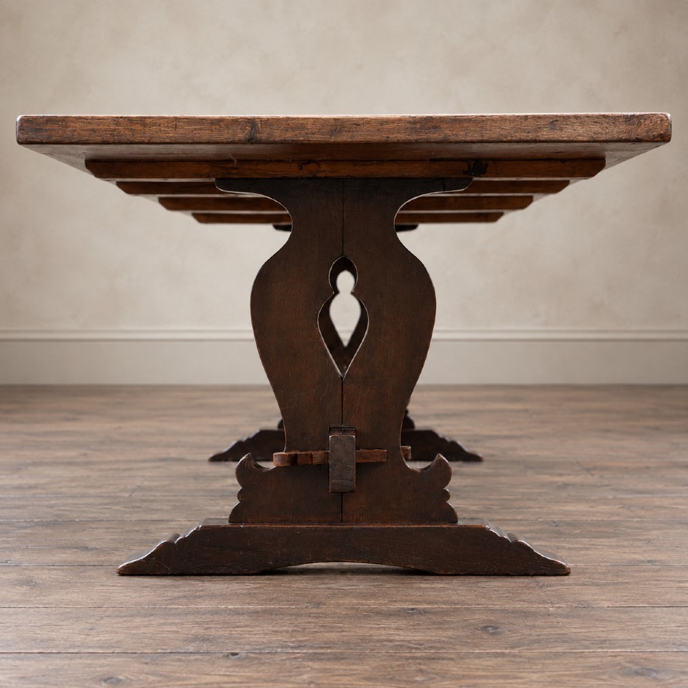 An early twentieth-century dark oak refectory dining table featuring a plank top, pierced trestle end supports, and a central connecting stretcher. View X