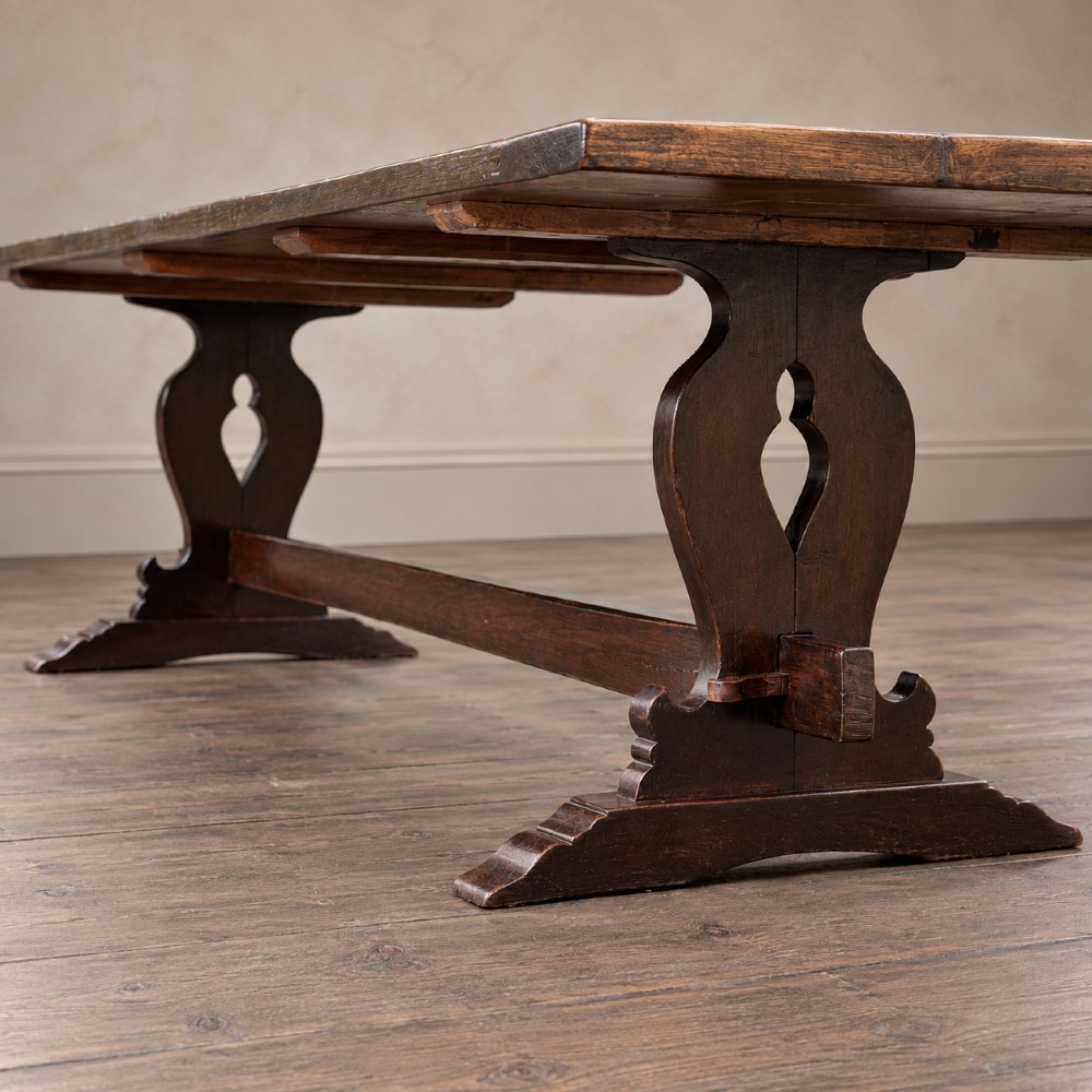 An early twentieth-century dark oak refectory dining table featuring a plank top, pierced trestle end supports, and a central connecting stretcher. View XI