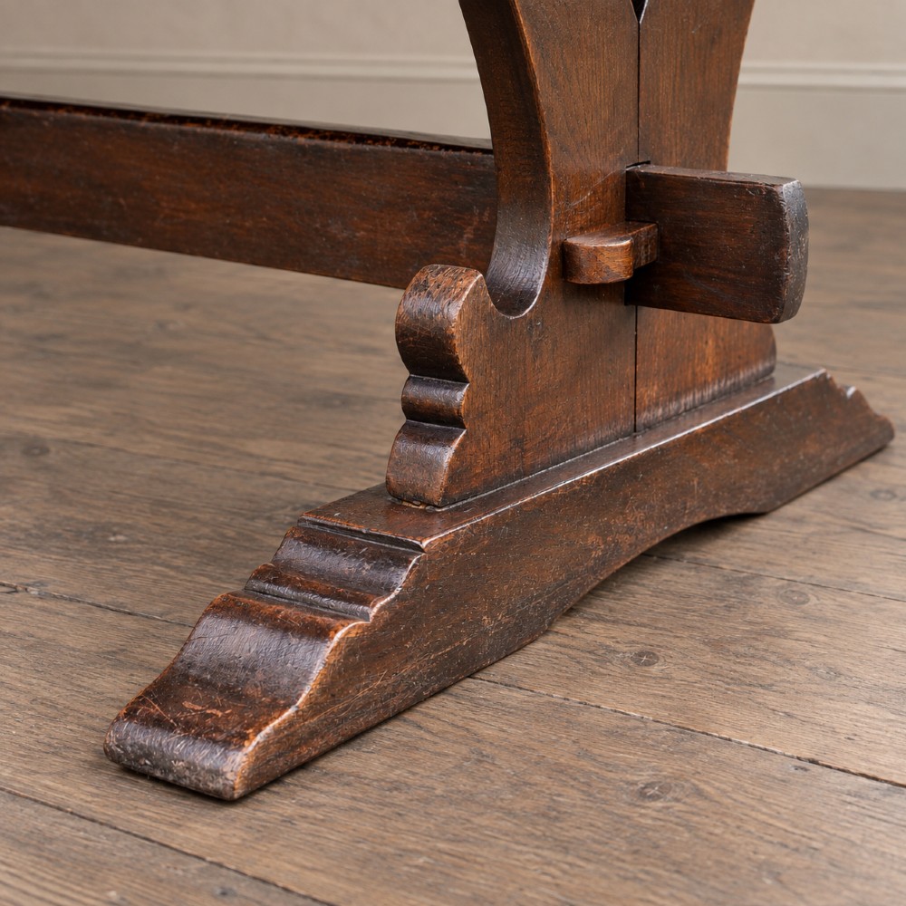 An early twentieth-century dark oak refectory dining table featuring a plank top, pierced trestle end supports, and a central connecting stretcher. View XIII